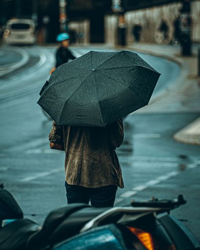 A vertical shot of a back view of a woman with a black umbrella standing in the street on a rainy day