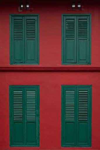 A vertical shot of windows with green frames on red wall background