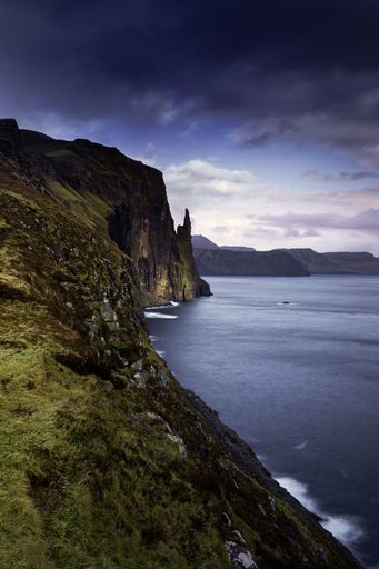 A vertical shot of the rocky formations near the beach on a clouded sky