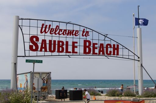 Sauble Beach, Ontario / Canada, August 9, 2020: Sign with red letters at the entrance to Sauble Beach with people and water in background