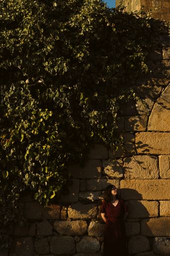 A vertical shot of a young caucasian lady standing near a brick wall in the Castle of Longroiva
