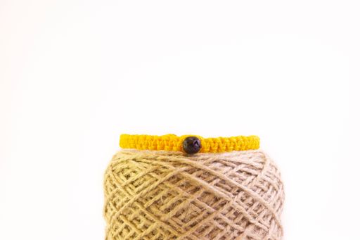 A close-up shot of a yellow handmade bracelet on a burlap thread isolated on a white background