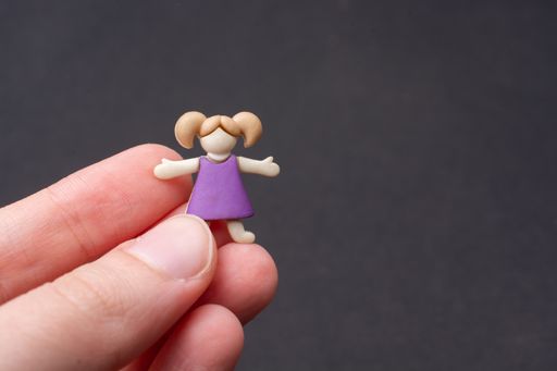 A macro closeup shot of a person's hand holding a miniature figurine of a girl on a gray background