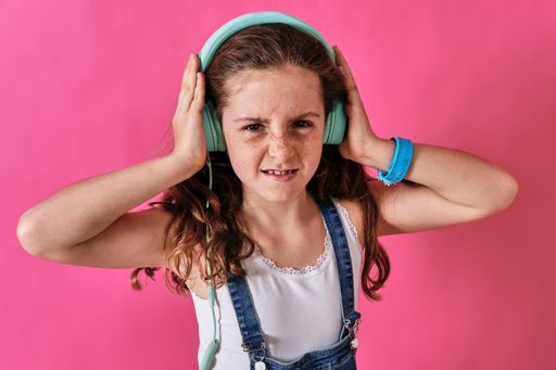 A little girl listening to music with headphones with a displeased expression