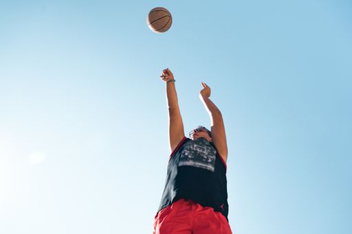 A low angle shot of a male player playing basketball with the clear blue sky in the background