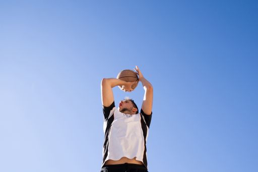 A low angle shot of a male player playing basketball with the clear blue sky in the background
