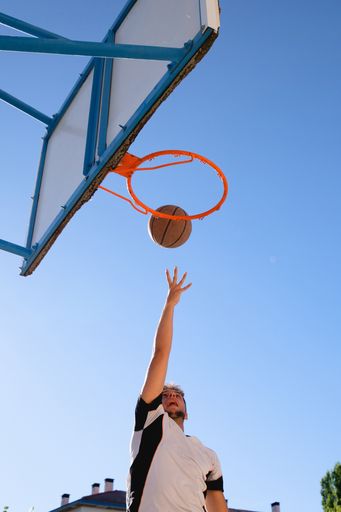 A vertical shot of a male player playing basketball with the clear blue sky in the background