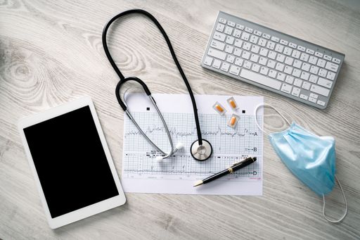 A high angle shot of a stethoscope, a tablet, pills, medical mask, cardiogram and keyboard on a wooden surface