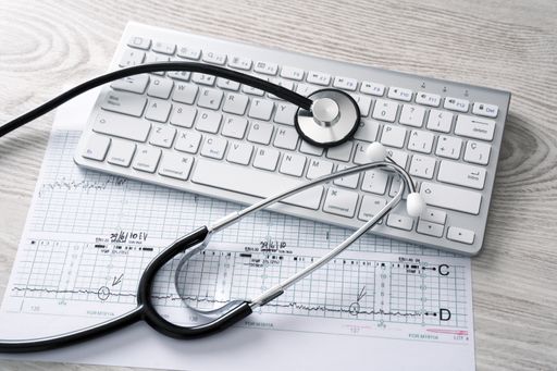 A closeup shot of a stethoscope, cardiogram and a keyboard on a wooden surface