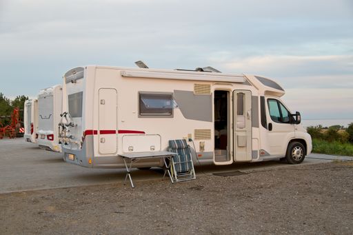 The rear and right sides of a white motorhome parked along with similar motorhomes