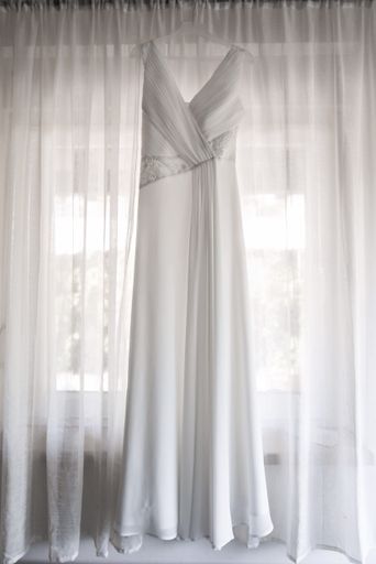 A vertical shot of a beautiful wedding dress hanging on white curtains