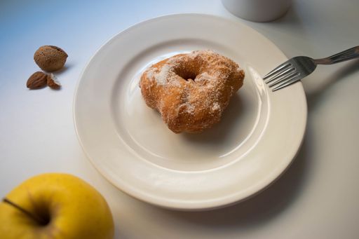 A shot of a donut on a plate, fork, apple and almond on the table