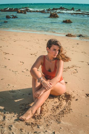 A vertical shot of a beautiful European female with an orange swimsuit sitting on sandy beach