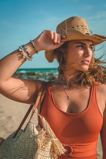 A vertical shot of a European female with an orange swimsuit and a cowboy hat posing on sandy beach