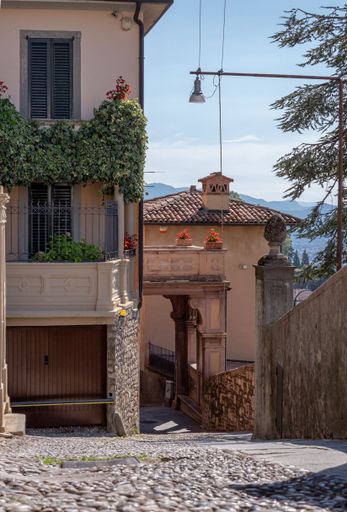 A vertical shot of a building and a rocky alley next to it in San Vigilio in Bergamo, Italy