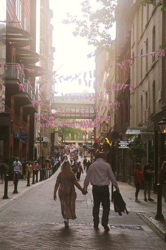 A vertical shot of the lovers walking in the crowdy streets with tall buildings and flags of London