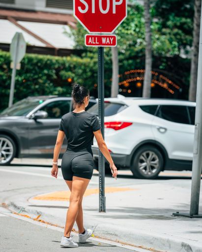 A vertical shot of a young female in athleisure crossing a road near a stop sign