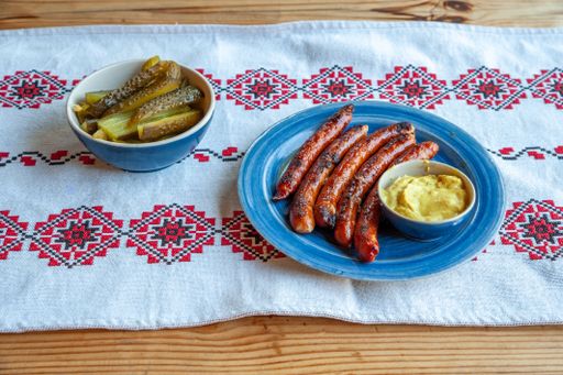 A beautiful shot of grilled sausages, potato puree, pickles in clay dishes placed on Russian embroidery tablecloth