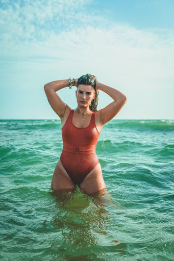 A vertical shot of a beautiful European female with an orange swimsuit posing at sea