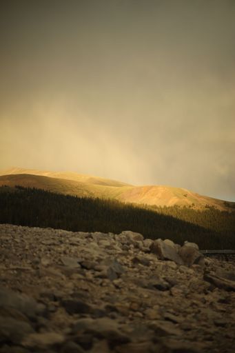 A vertical shot of of hills surrounding a forest with lush nature in cloudy sky background