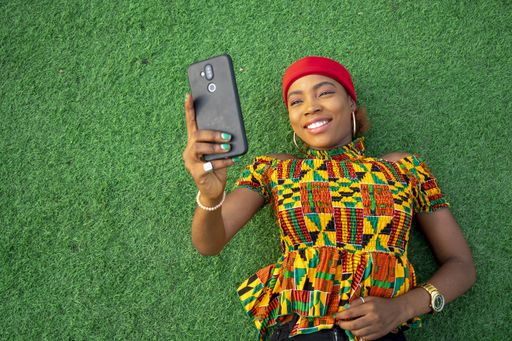 A beautiful young black female laying on the floor in a park using her mobile phone