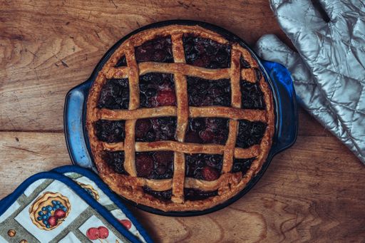 Homemade pie on wooden table with kitchen equipment around it.