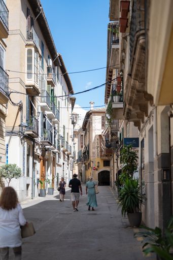 A vertical shot of a narrow street with people walking in Palma, Mallorca, Spain