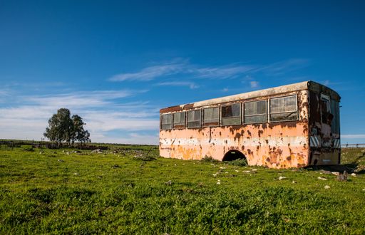 A beautiful view of an old abandoned bus in a green field under cloudy sky