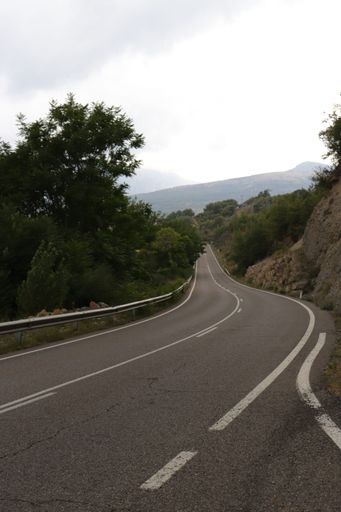 A vertical low-angle of a road through rocky mountains, gloomy sky background