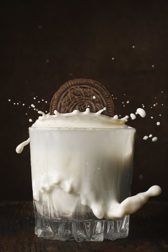 A vertical shot of a chocolate Oreo splashing into a glass of milk on a wooden background