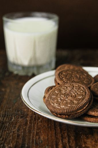 A vertical closeup shot of a plate of chocolate filled Oreos and a glass of milk in the background