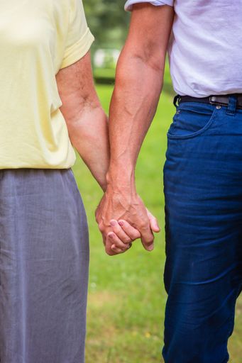 A vertical shot of a couple holding hands touching with blur garden