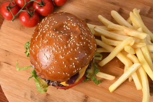 A top view of a delicious beef burger on a wooden board with french fries and tomatoes on it