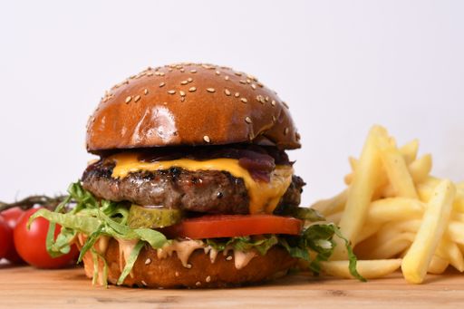 A closeup shot of a juicy beef burger, french fries, and tomatoes on a table