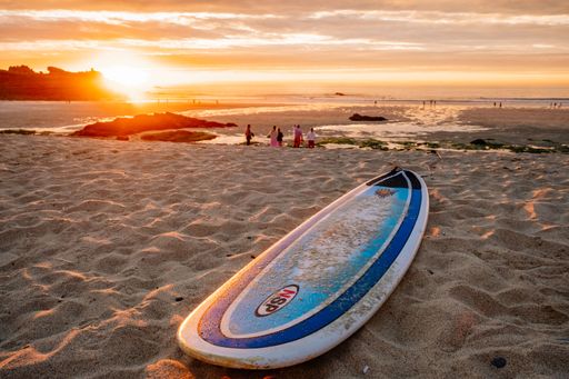 A closeup shot of a surfboard on sandy beach at sunset