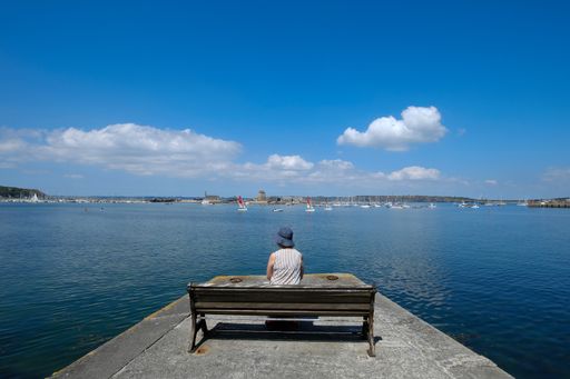 A person sitting on a bench on the pier looking out into the sea and the clear blue sky