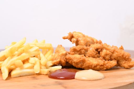 A closeup shot of chicken strips, french fries, tomatoes, and sauces on a wooden board
