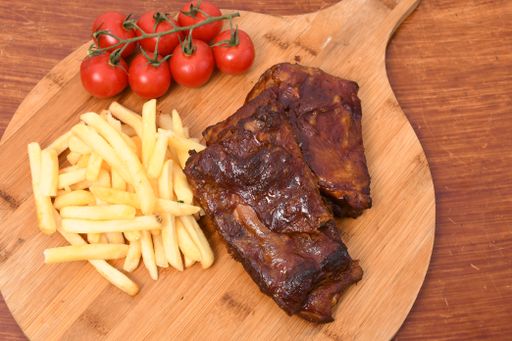 A high angle shot of meat slices, french fries, and tomatoes on a kitchen board