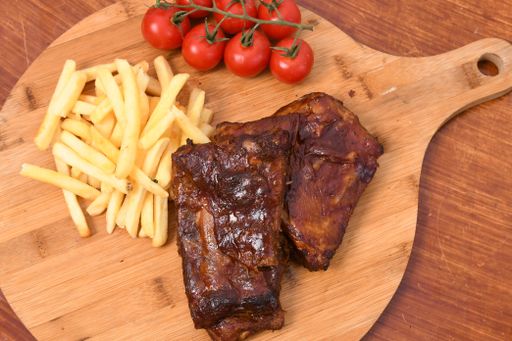 A high angle shot of roasted meat on a wooden board with french fries and tomatoes on it