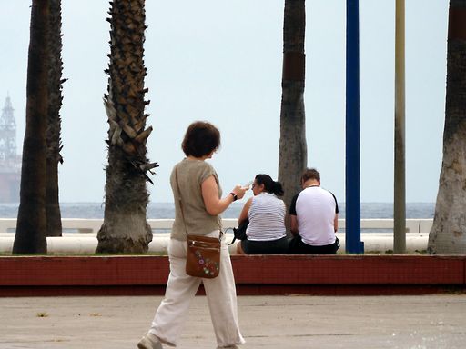 A woman walking happily near a couple resting on the street by the sea with palm tree