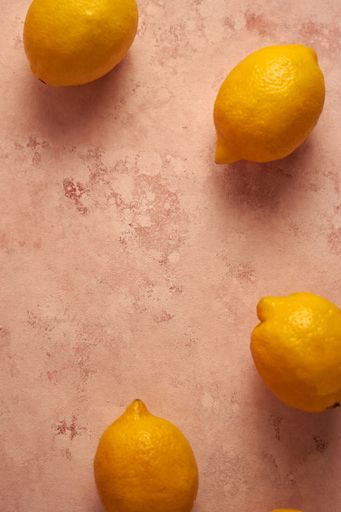 A vertical top view of lemons on a pink marble table