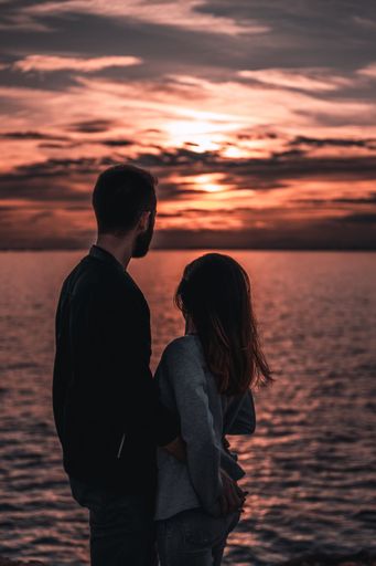A vertical shot of a loving couple hugged watching a colorful sunset on a shore