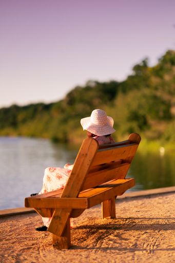 A woman sitting on a wooden bench while looking at a calm lake during sunset