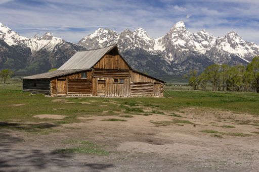 The view of an old wooden house in greenery before the snow-covered mountains