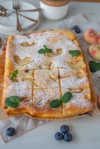 The high-angle vertical view of a homemade peach pie with blueberries and ricotta on a white table