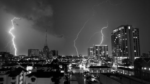 A grayscale of striking lightning at night in an illuminated city of Phoenix, Arizona