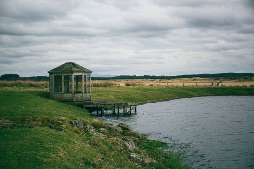 An old wooden structure and a small pier over a lake under a cloudy sky