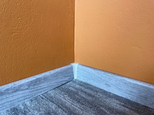 Carpet with plastic baseboard with a wooden texture. Newly installed wooden grey carpet flooring and baseboards in home. Modern design.