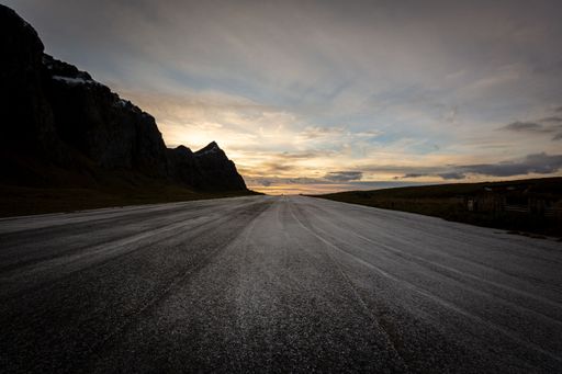 The countryside road by the mountains under the cloudy sky at sunset