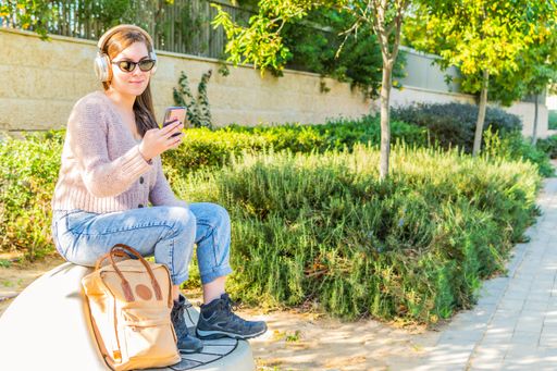 A Caucasian female watching videos on her smartphone with headphones and sitting in a park